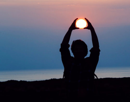 Man in darkness with hands help up to surround the sun