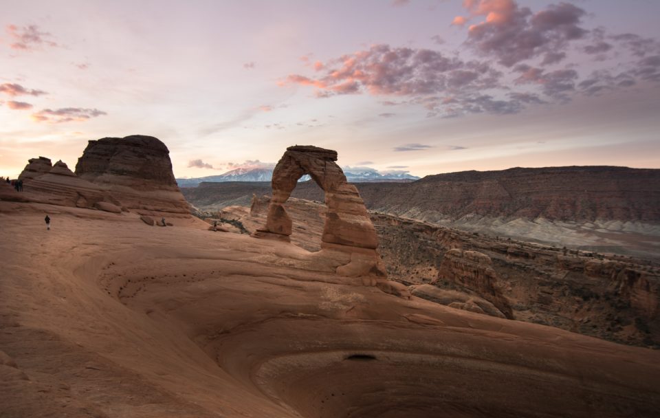 A lone person walking toward a rock arch in the desert